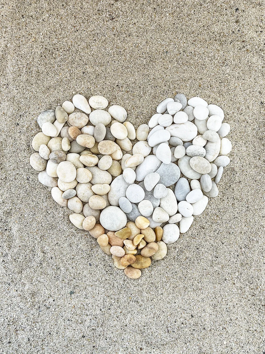 A heart shape made of small, smooth white and tan pebbles on sandy ground.