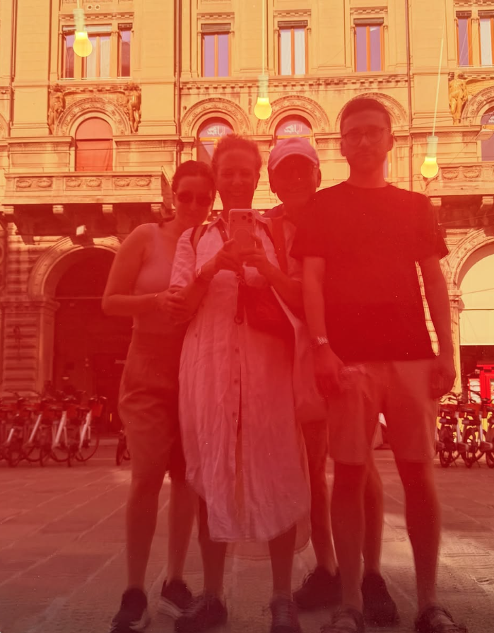 Four people standing together in front of a historic building, taking a selfie, with bicycles parked behind them.