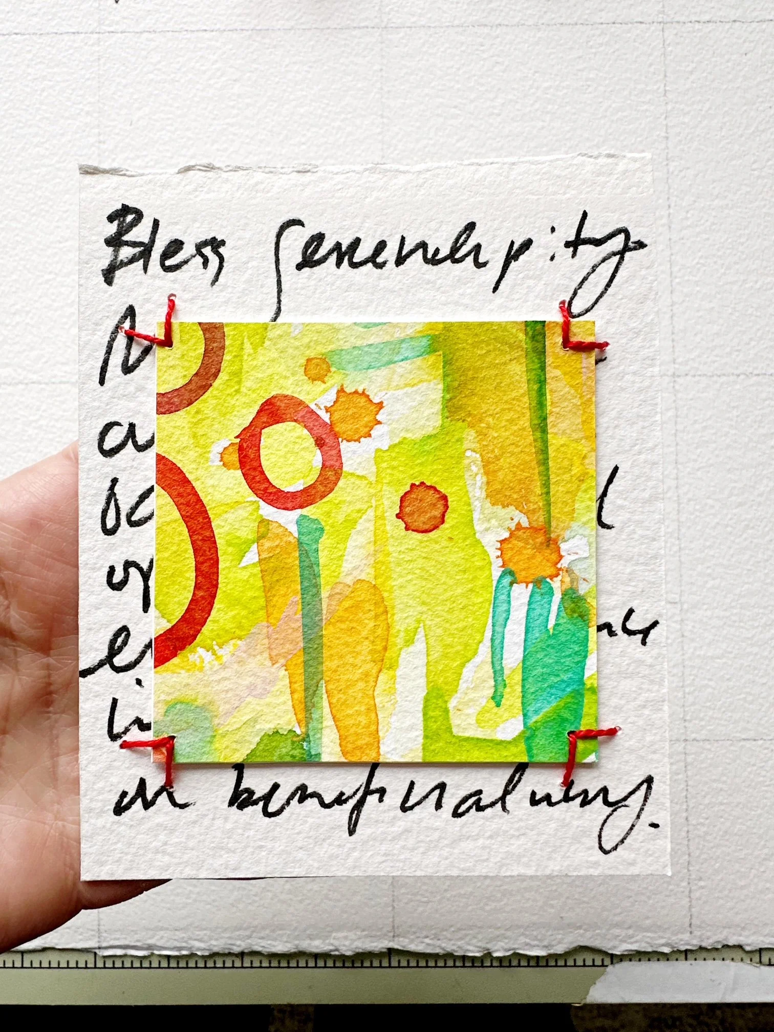 Colorful abstract watercolor painting with orange, red, yellow, green, and blue splashes on a white background, attached to handwritten notes with red stitches.