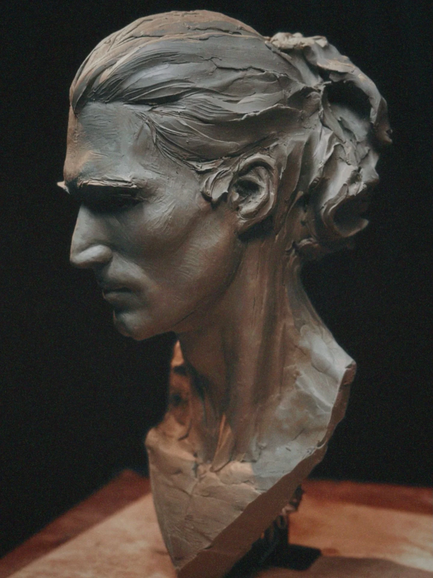 A sculpture of a woman's face in profile with detailed hair and closed eyes, mounted on a piece of stone or marble.