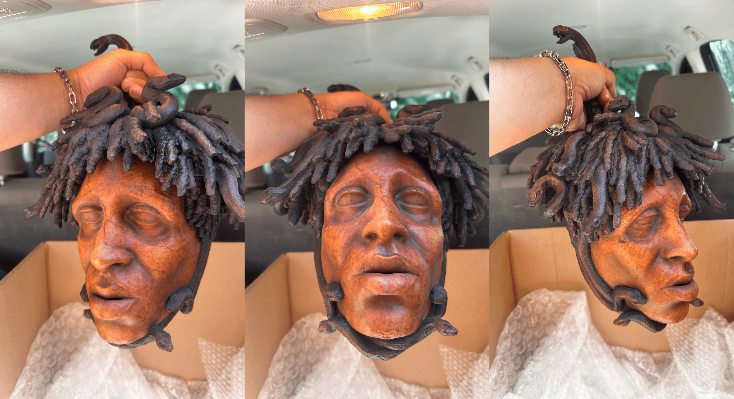 A sculpture of a person's head with dreadlocks, made from a brown, textured material, displayed inside a cardboard box with packing material surrounding the base.