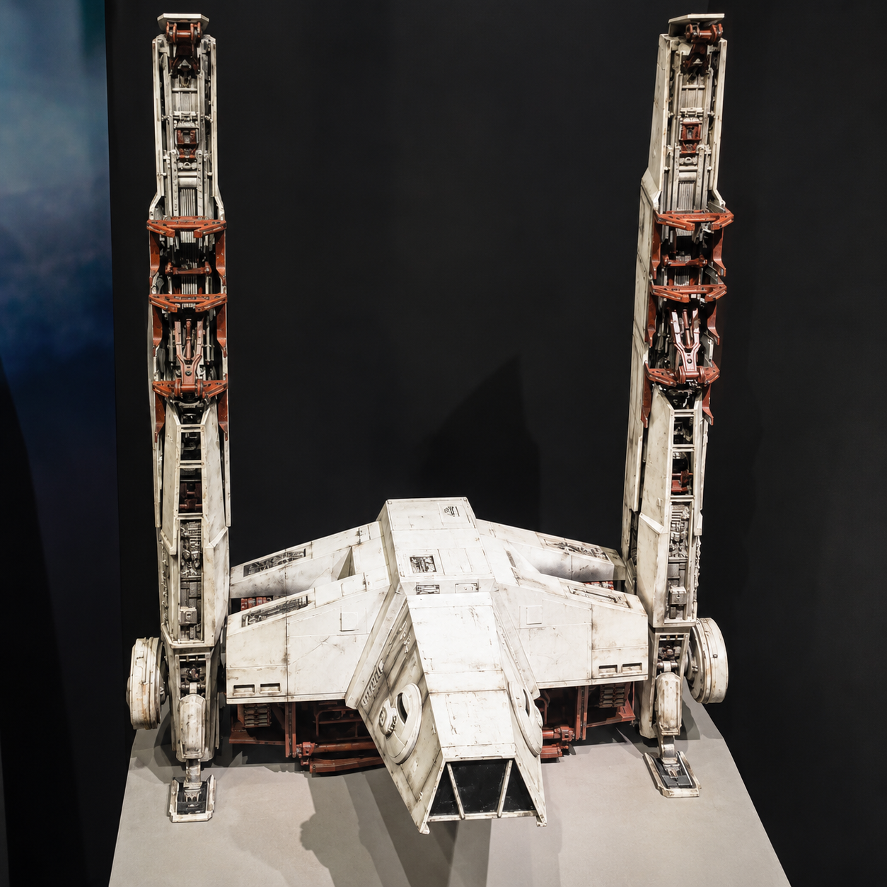 A detailed model of a spaceship with tall vertical structures on each side, resembling wings, painted mostly white with some red and black accents, set against a dark background.