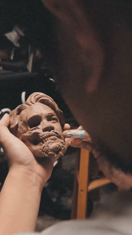 Person sculpting a detailed clay bust of a man's face.