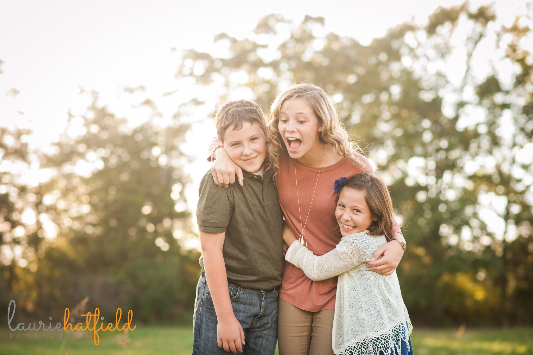 brother and 2 sisters laughing in a field | Mobile child photographer