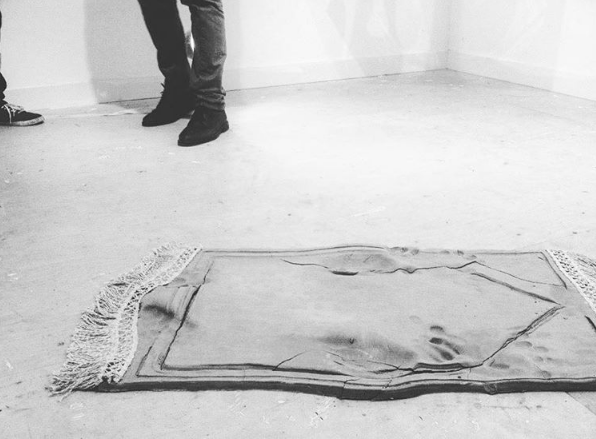 ‘Imprints’ is a sculptural installation depicting a Muslim prayer mat. In Islamic tradition, a Muslim is obliged to perform the prayer ritual |Salah| five times a day, in which one humbles themselves in front of Allah through various actions including prostration. The sculpture is marked by the imprints left behind after a person's performance of the Salah. Made from raw clay, the material is symbolic of the Islamic belief that man and woman are created from clay. The organic and pure nature of the piece is a further allegory of the spiritually purifying conduct of worship. The artwork faces the Qiblah, the direction towards which all Muslims pray.