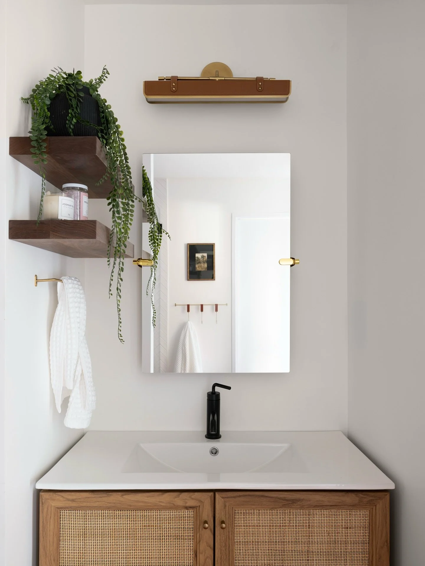 Elevate your bathroom with texture and warmth ✨ This 1970s-inspired rattan vanity brings organic charm and midcentury flair to the space. The floating shelves keep the area open and functional and a leather light fixture adds a warm, retro touch. Rea