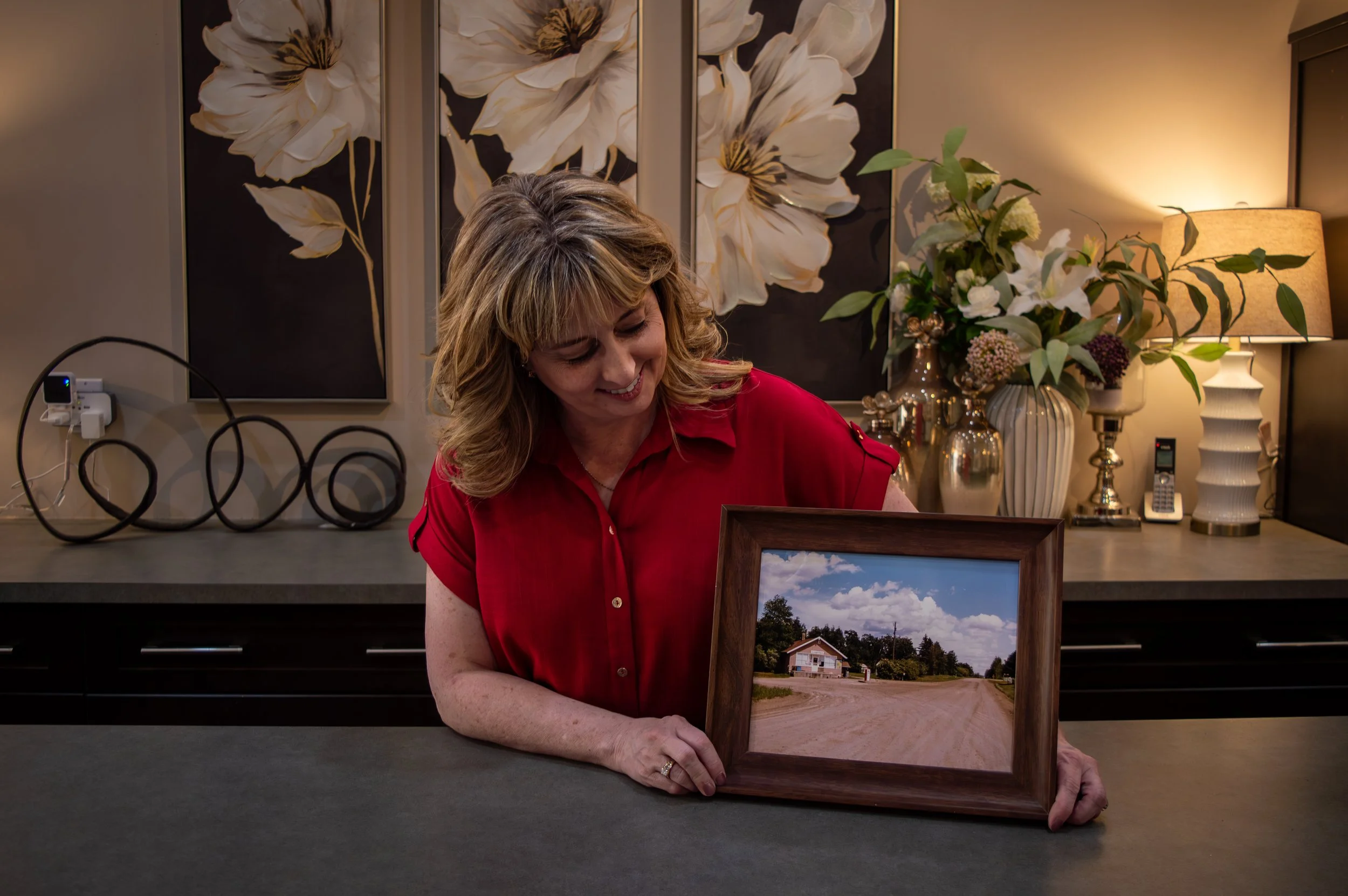 Dara in a red blouse inside Dara's, looking down at a framed photo of the Lunnford General store.