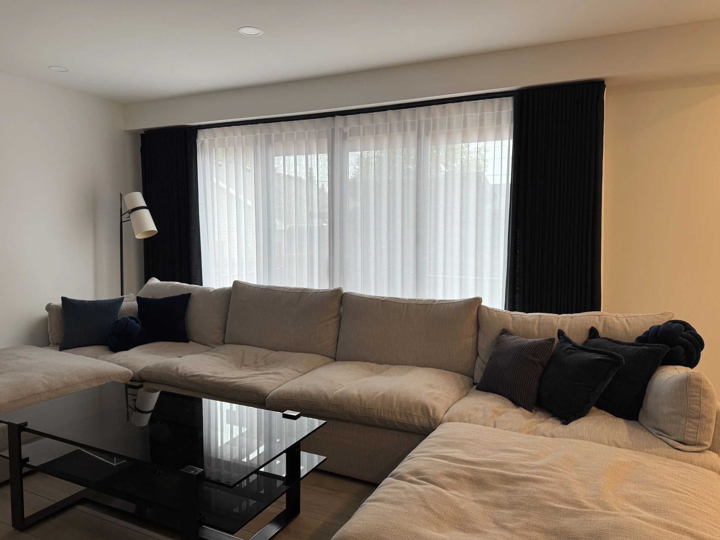 Black curtains and light sheers fitted over a living room window.