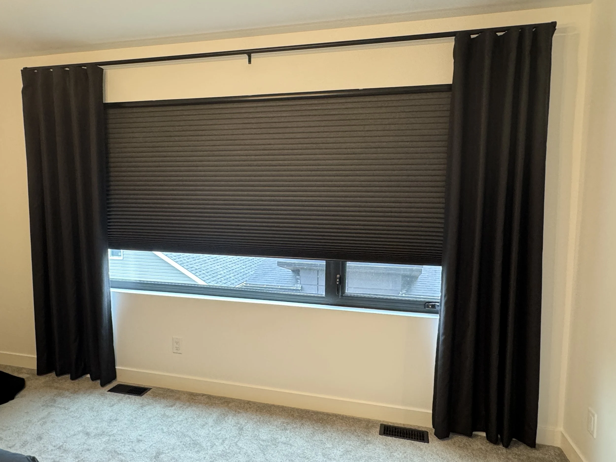 Black blinds and dark drapes fitted on a bedroom window.
