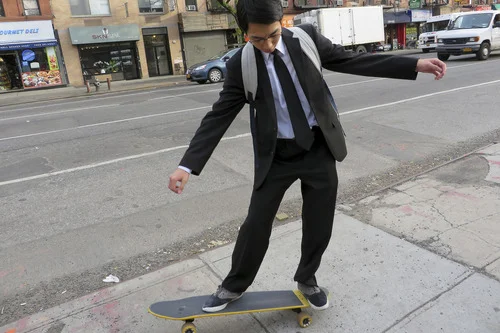 A young professional rides a skateboard to work in his suit.