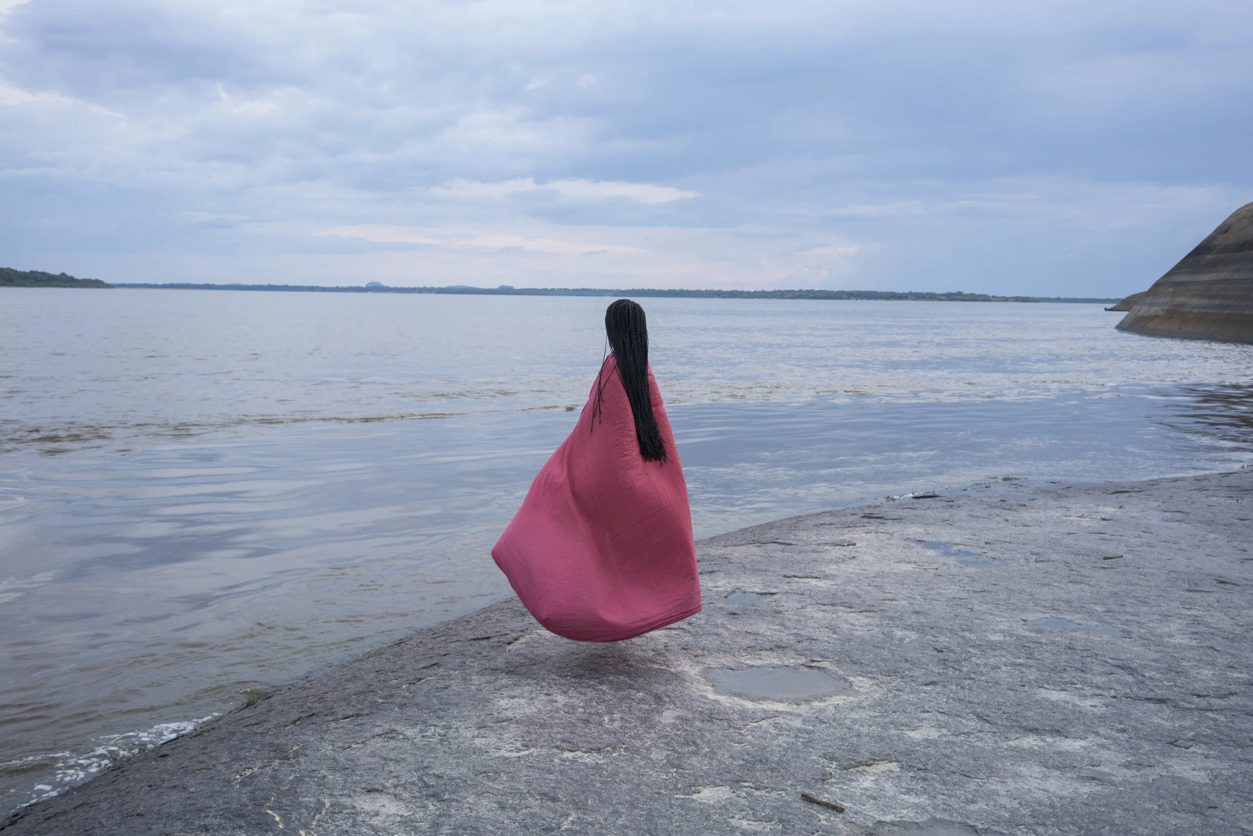 Juanita Escobar. Liz at the Orinoco River’s tepui rocks, looking towards Venezuela. Liz was born in Choco, at the Colombian Pacific coast, at an early age she moved with her mother and sisters to Puerto Ayacucho, Venezuela. A year ago, she had to leave to come back to Colombia with her two sons, leaving her mother and sisters. More than the sense of missing her family, she worries whether her mother and sisters have enough to eat on the other side of the river. On this day, Liz was with her two sons at the river. During the dry season, people go to the beaches; in the winter, the rocks are covered by the water. Puerto Carreño, Vichada Department, Colombia, 2017.