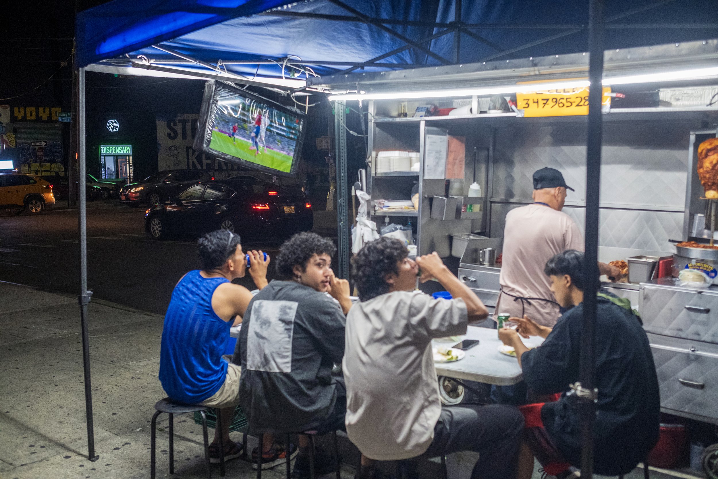 A street vendor grills tacos al pastor while World Cup fans watch the Mexico vs Czechia match outside the Jefferson Street L train station in Bushwick, Brooklyn, on June 24, 2026. 