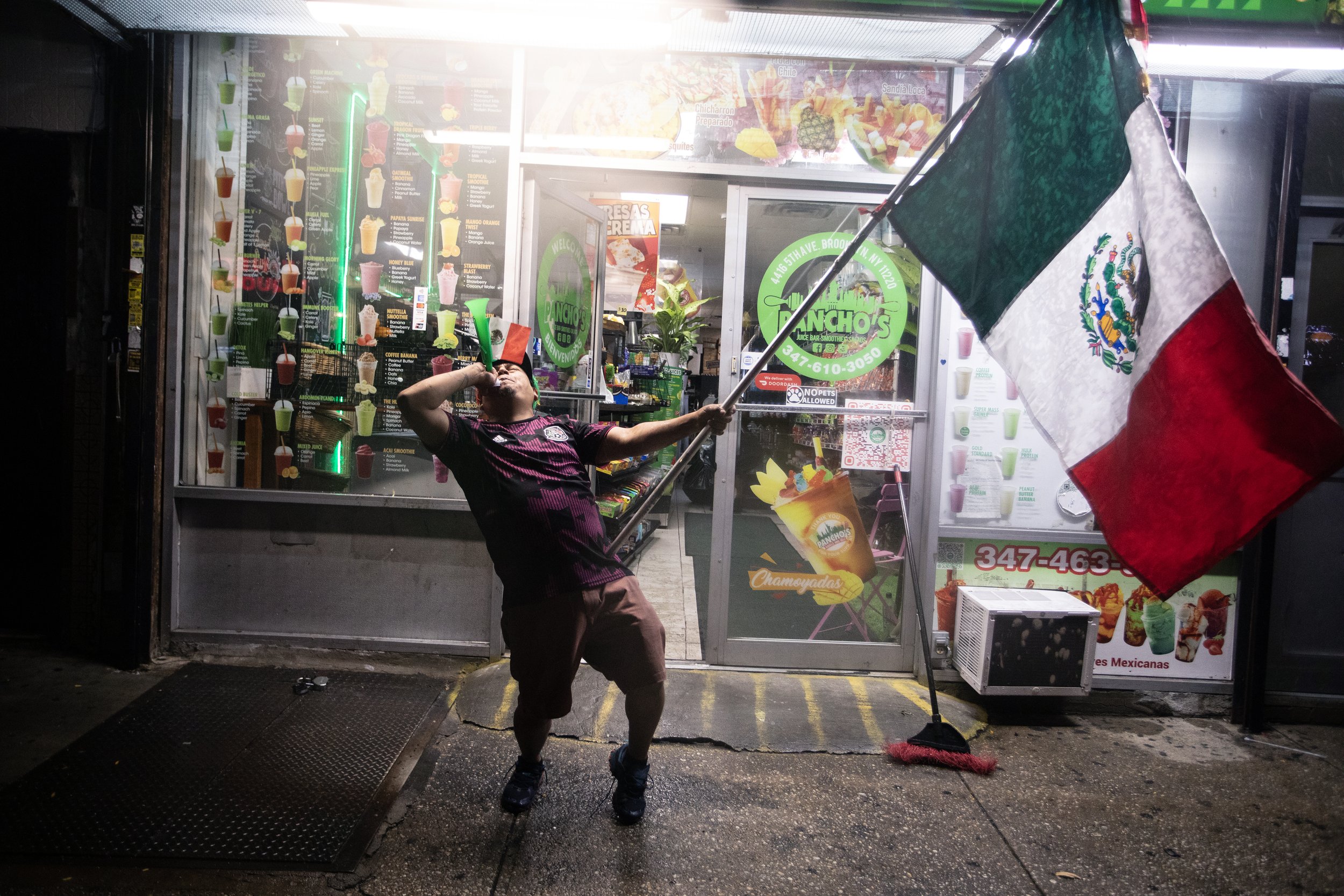  Fan blows a horn and proudly waves the Mexican flag during the Mexico vs. England match on the sidewalk in Sunset Park, Brooklyn, July 5 2026. 