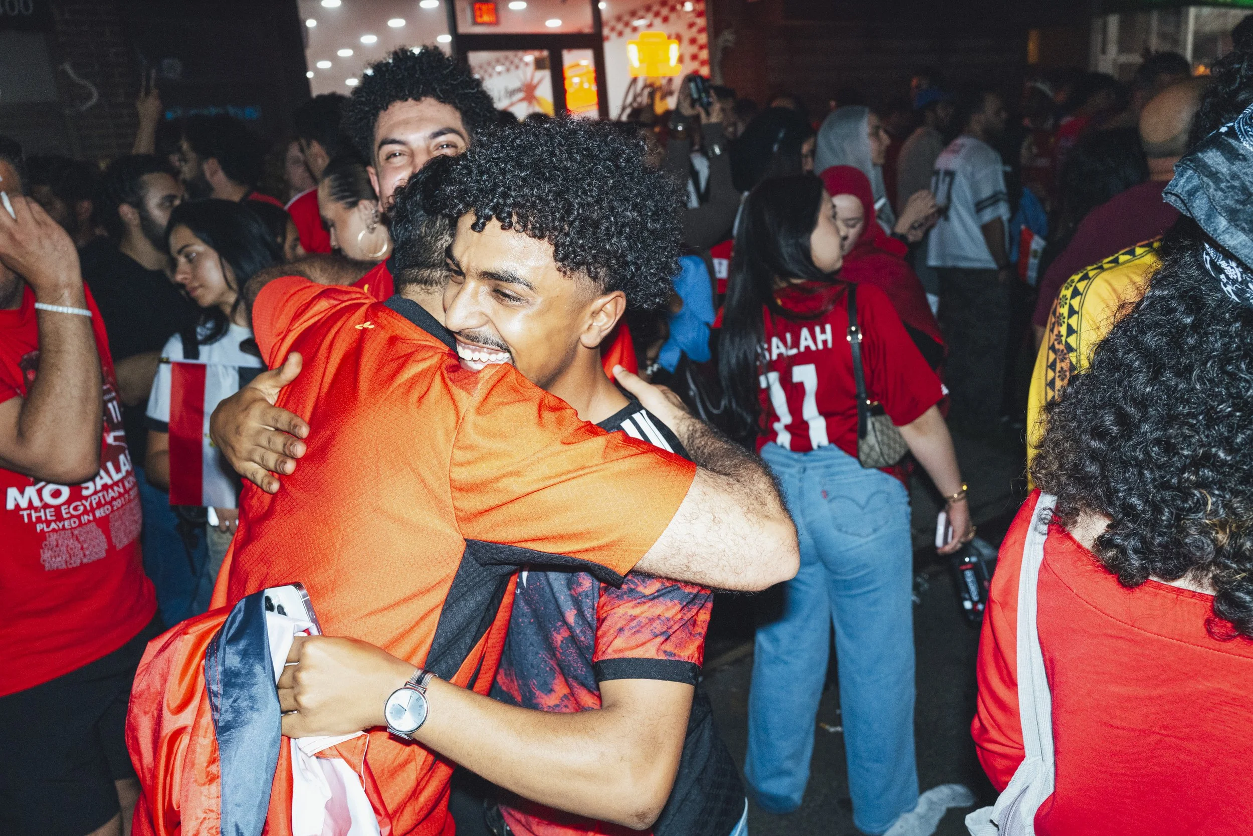  Two men hug on Steinway Street in Astoria, Queens, after the Egypt-Iran match on June 27, 2026. 
