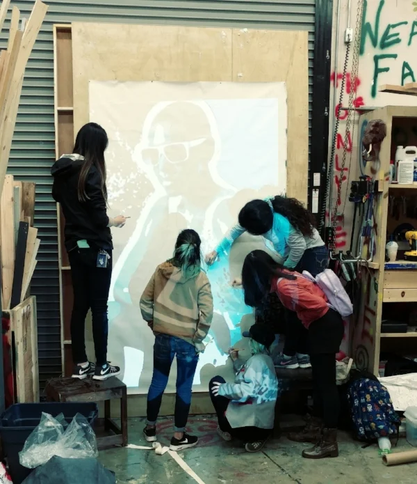 Students of the Oakland Tech Artesteem group along with the CCA student interns work on penciling in the image on canvas using a projector.