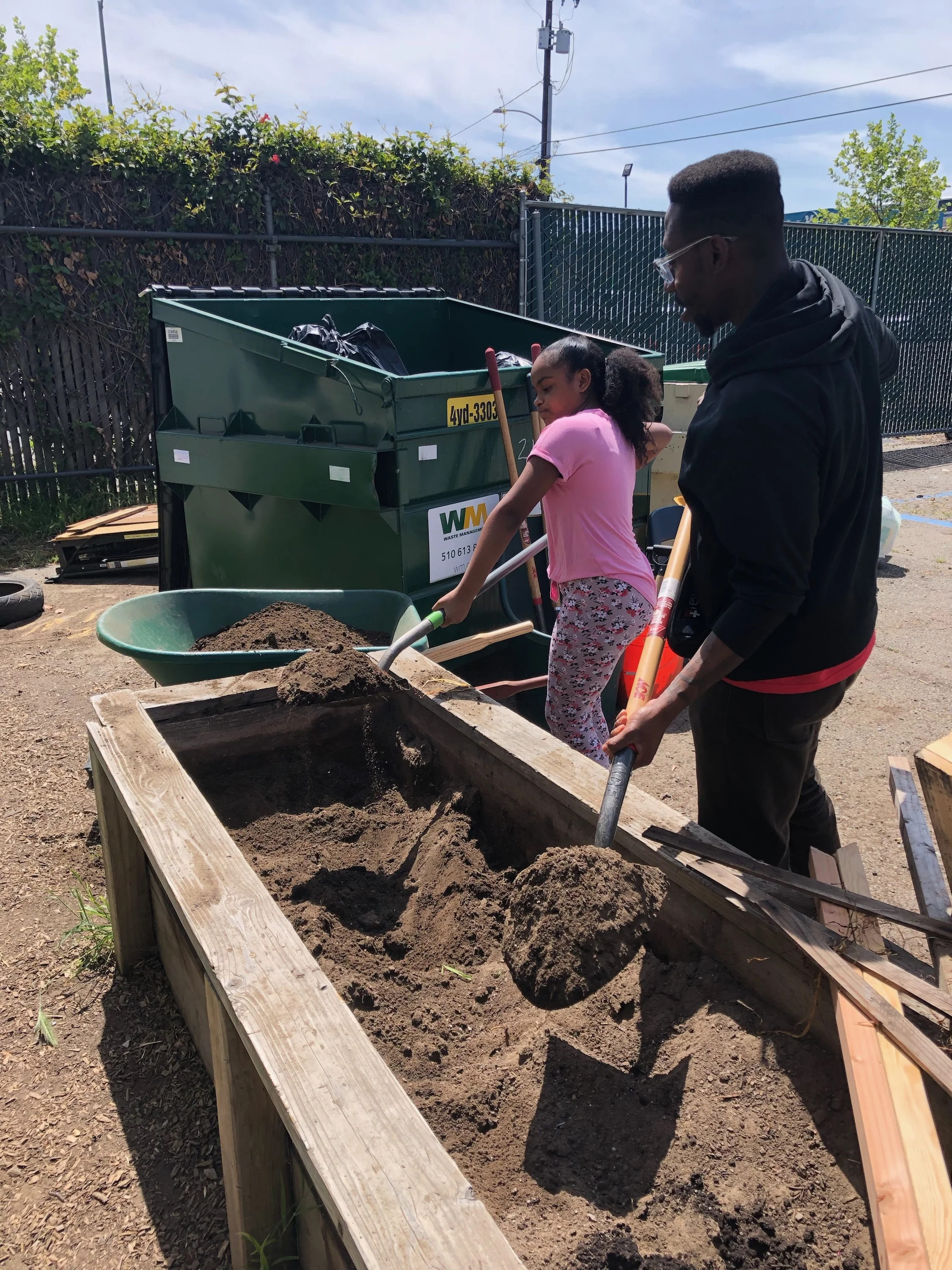 Staff member Malcolm, pictured to the right, assists a student shoveling new fertilizer into the planters-box.