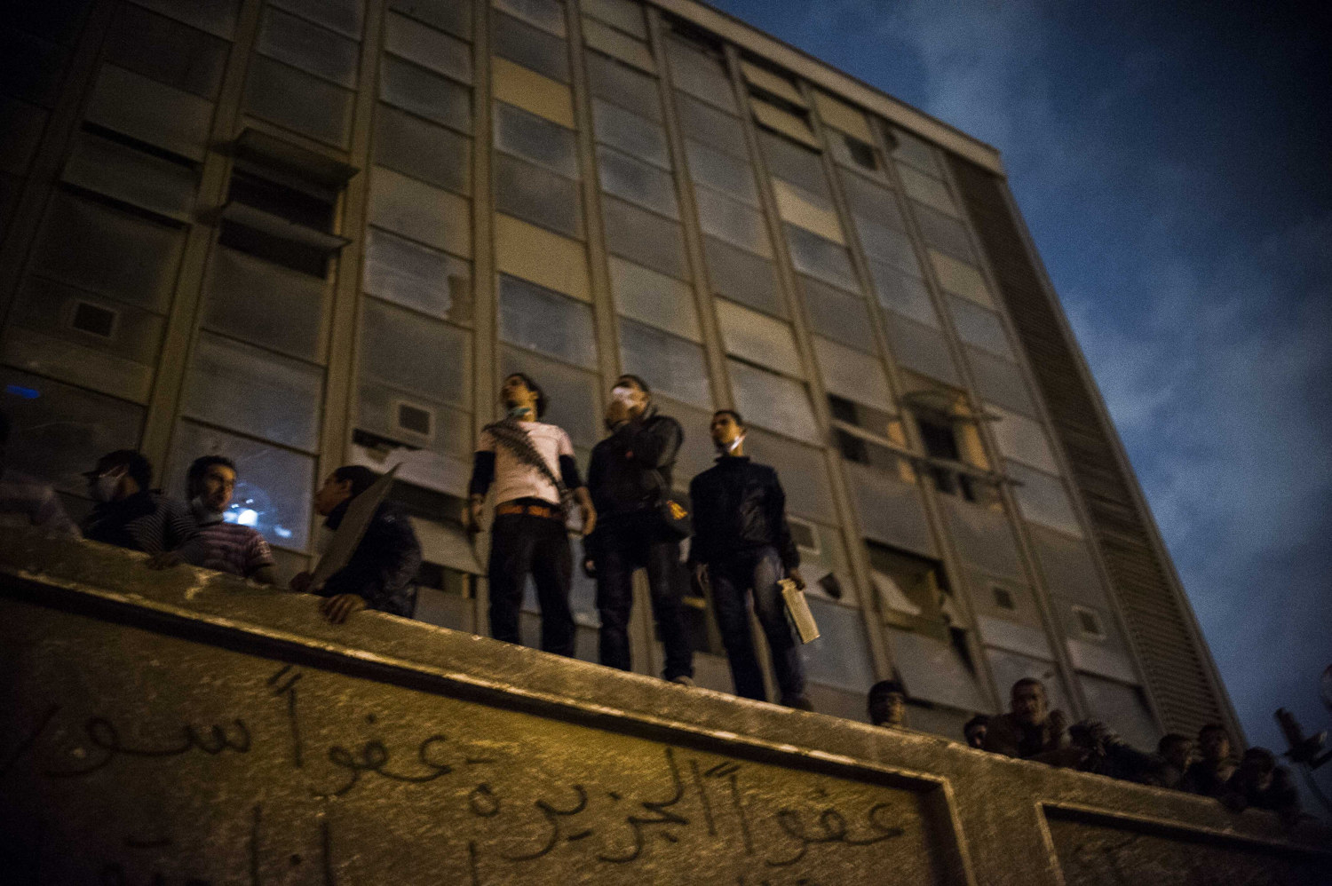  In November of 2011, Egypt is once again thrown into turmoil shortly before for the first democratic election. Men standing on the former American University in Cairo off Tahrir Square view the violent conflict between police forces and demonstrator