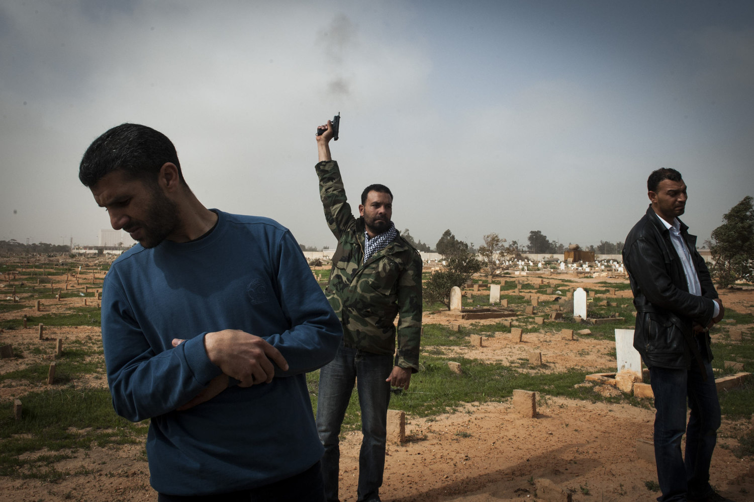  A man fires off a gun into the air to mourn. Men attend a mass burial at Benghazi Cemetery of seven men killed in an armory explosion the night before. It's not clear whether the armory exploded due to airstrikes or error by the soldiers. 