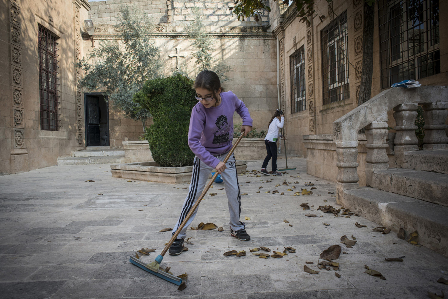  An Assyrian girl cleans up leaves in the courtyard of Mor Barsaumo before her Aramaic lesson on October 30th, 2014.
 