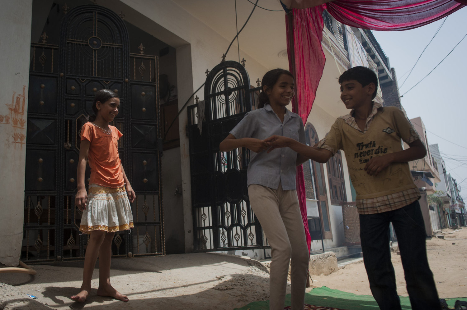  Two girls and a boy play outside in a funeral tent, set up for the local elder who has passed. 

 