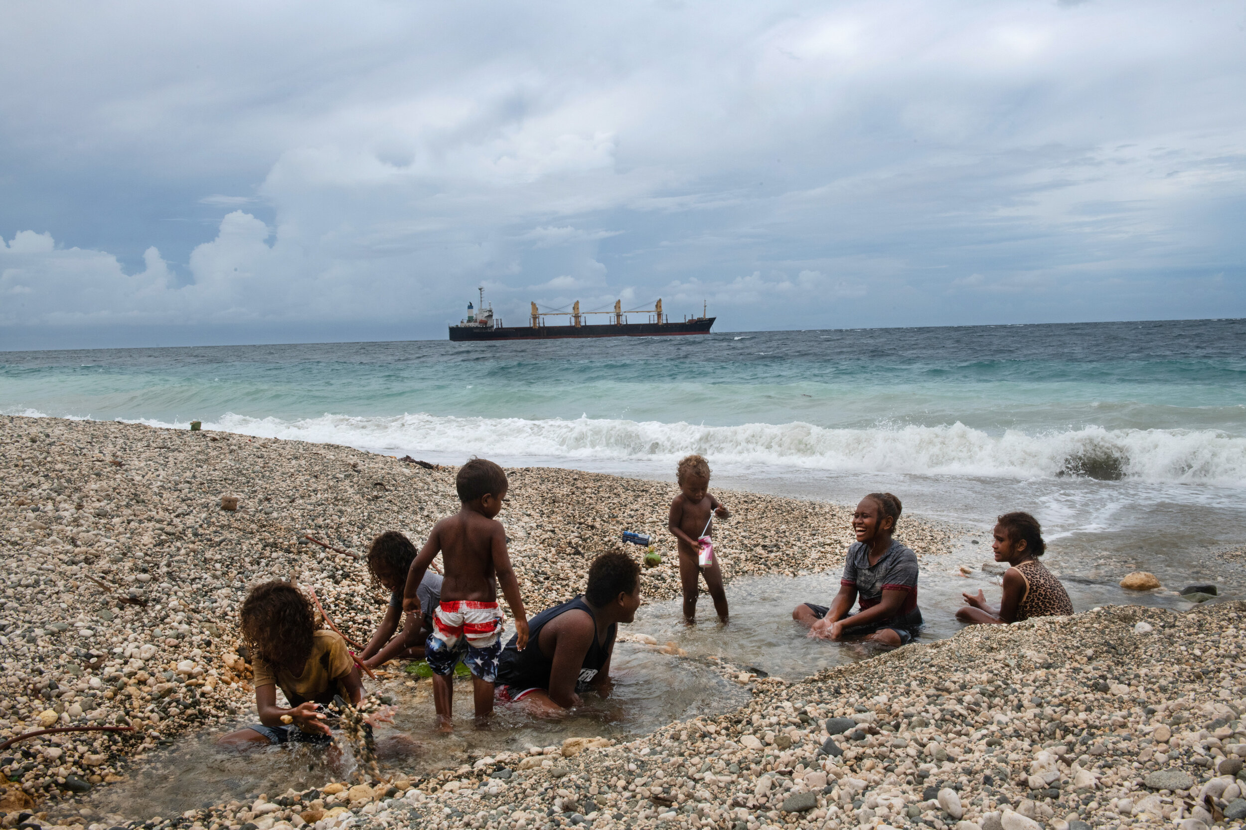  Children play on the beach outside of Honiara, in front of a logging ship waiting to be loaded on September 14th, 2019. Nearby is a logging point, which is at the end of the road and is where logs are loaded onto ships. Thousands of logging points d