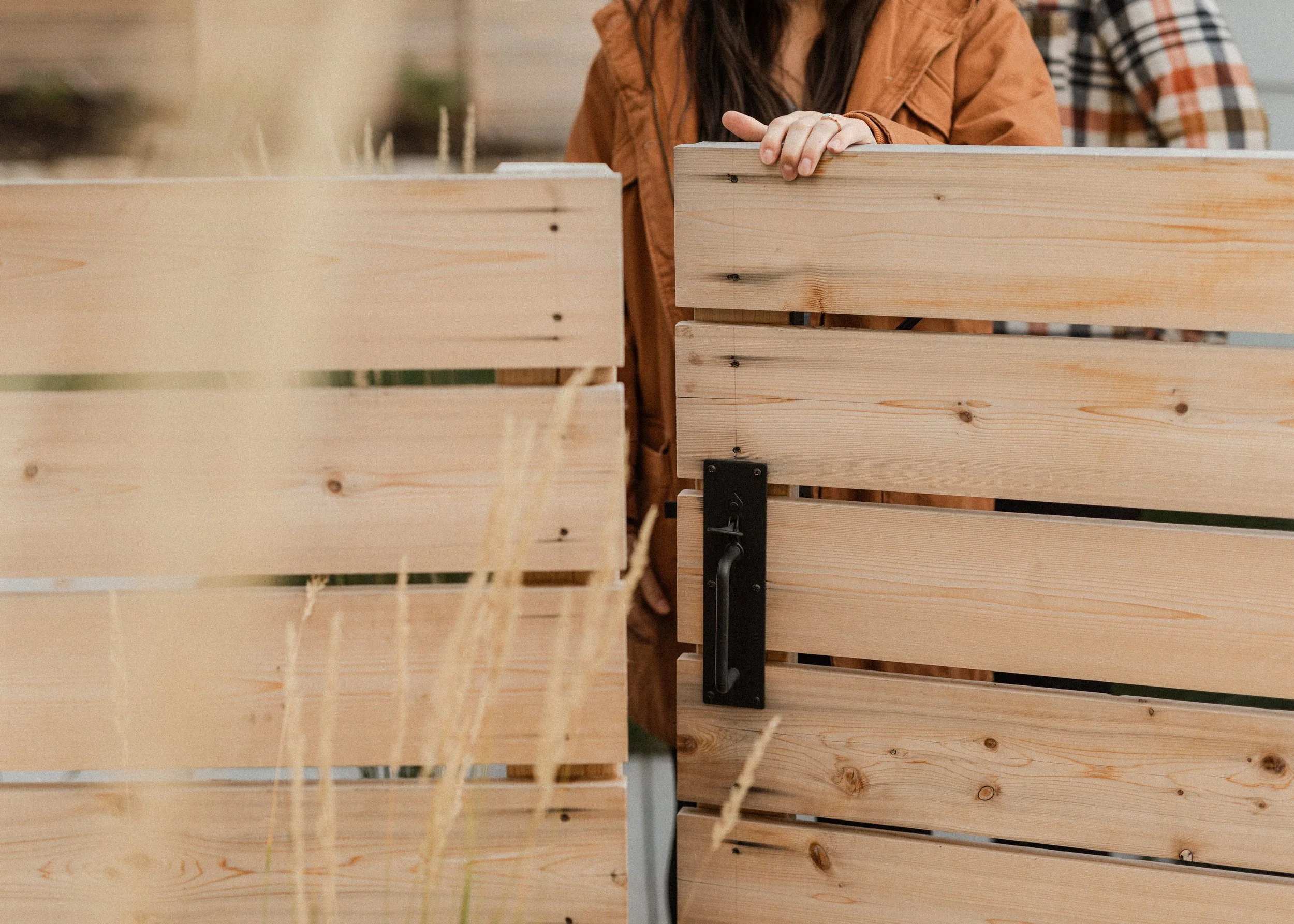 Close-up of a person wearing a brown jacket working with wooden planks, possibly in a woodworking or construction setting.