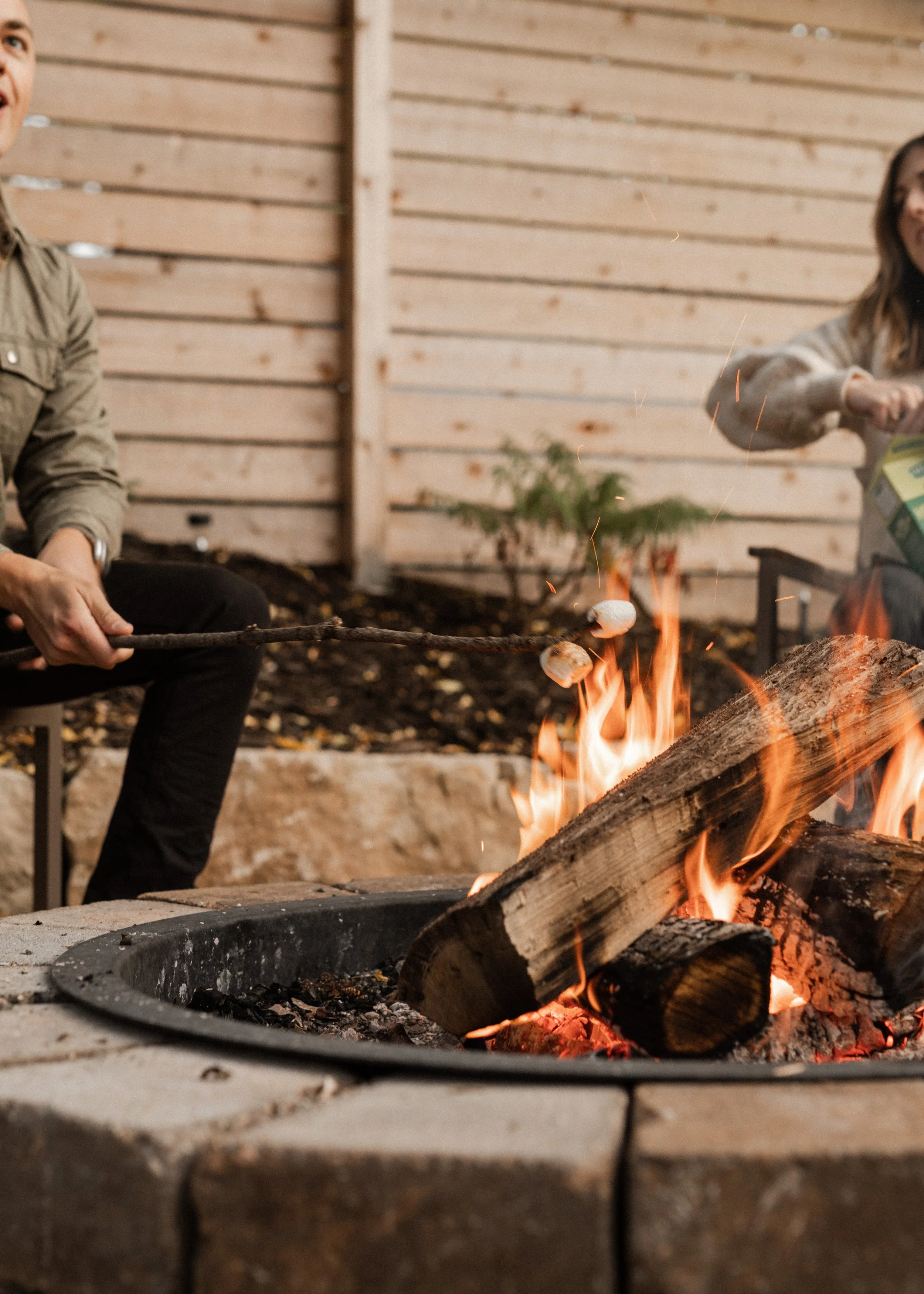 People sitting around a campfire inside a wooden structure, with visible logs and firewood in the fire.