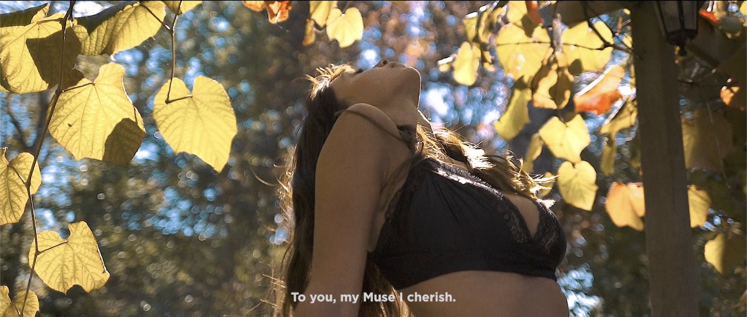 Femme avec des cheveux longs portant un haut noir, debout sous un arbre avec des feuilles jaunes en automne. Soleil brillant dans le ciel.