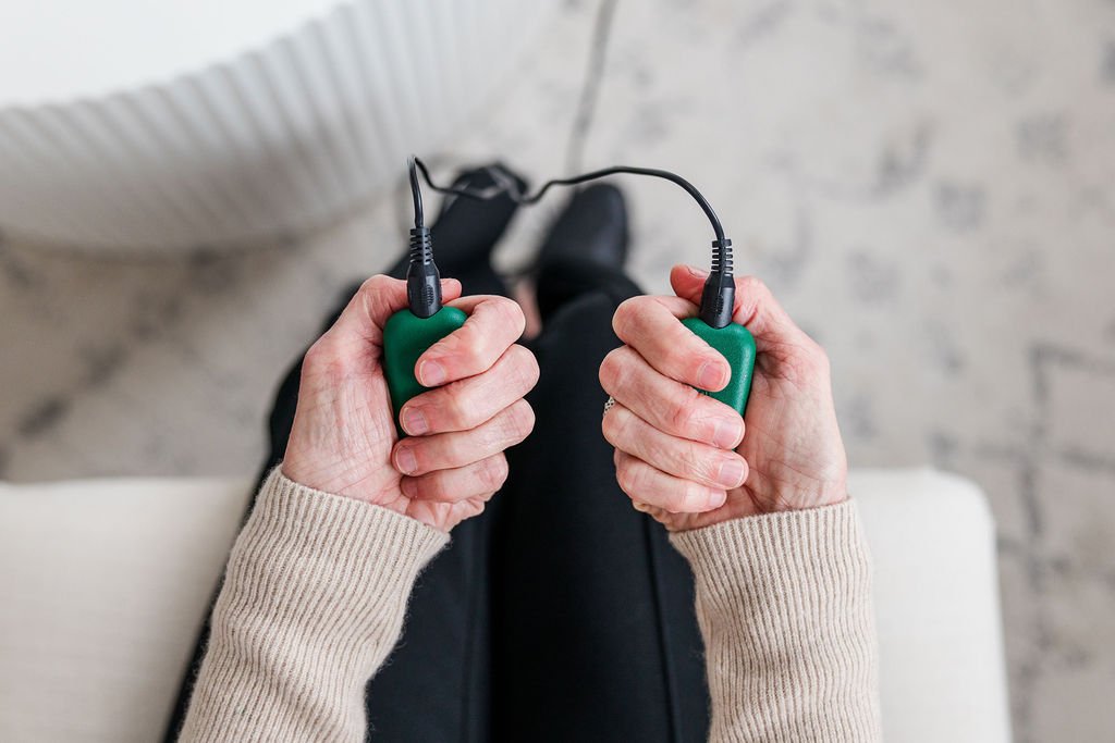 Person holding green hand grips with black wires attached, sitting on a white couch.