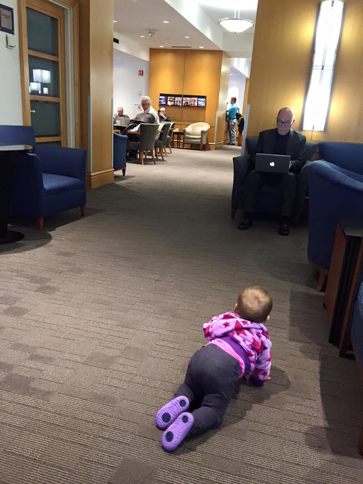 My daughter crawling around the Delta Sky Lounge while a business man is working