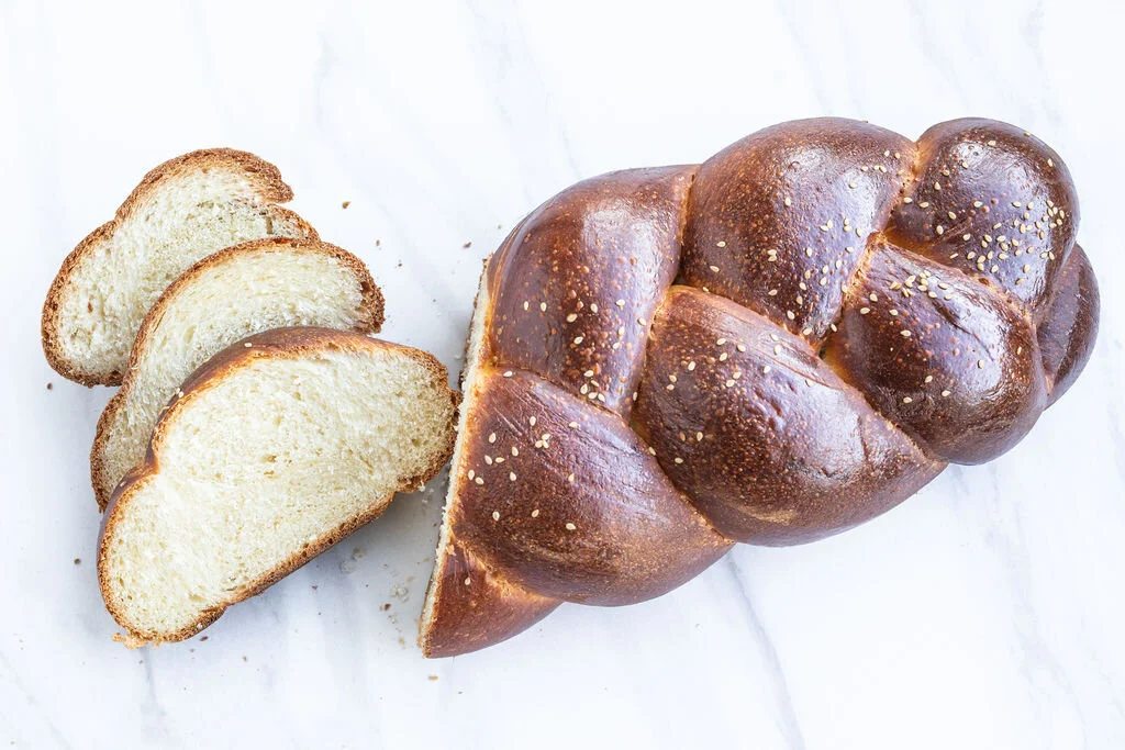 Loaf of braided bread with three slices cut and placed beside it, on a white surface.