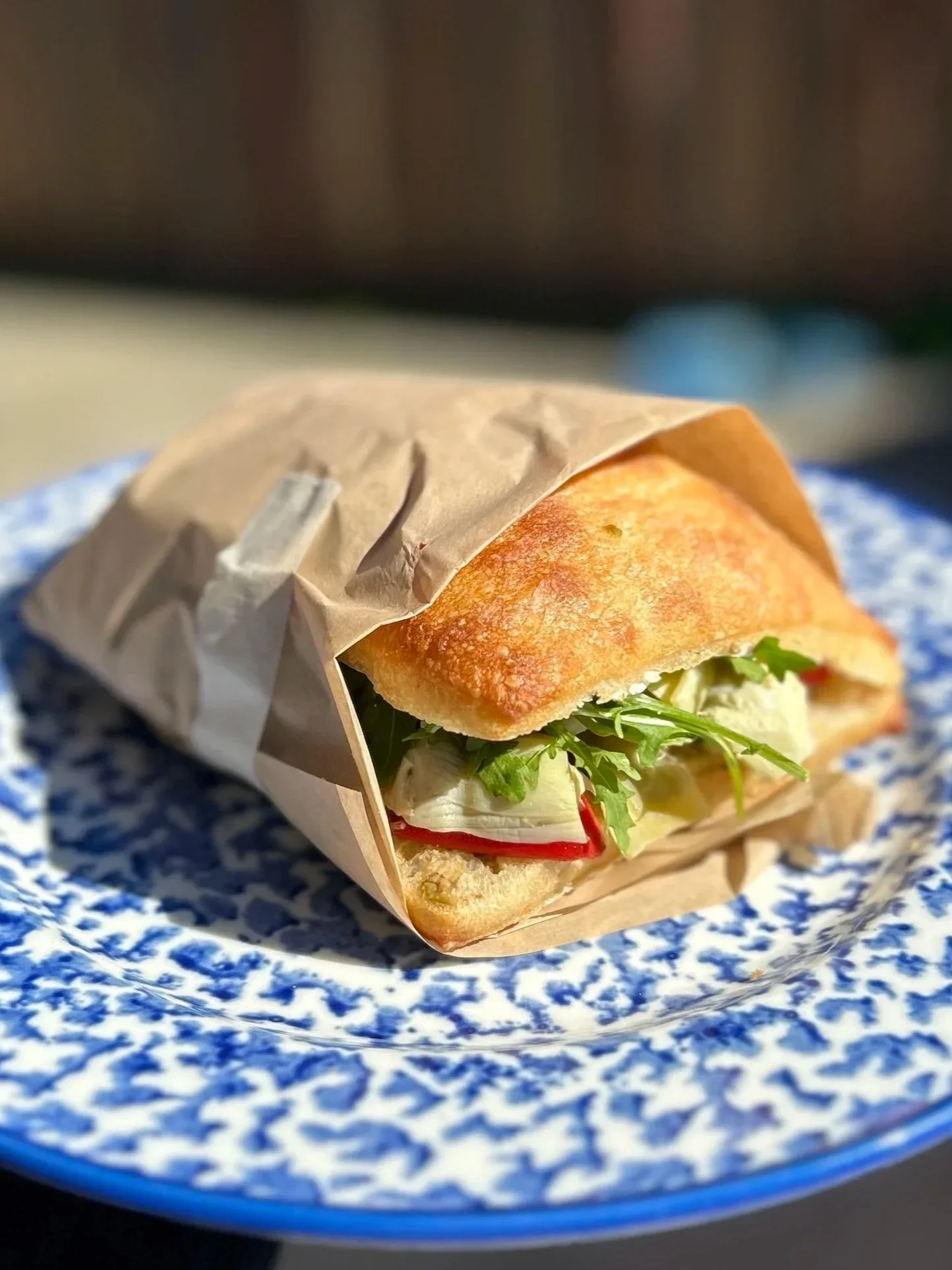Sandwich wrapped in paper with lettuce, tomato, and possibly turkey or chicken inside, served on a decorated blue and white plate.