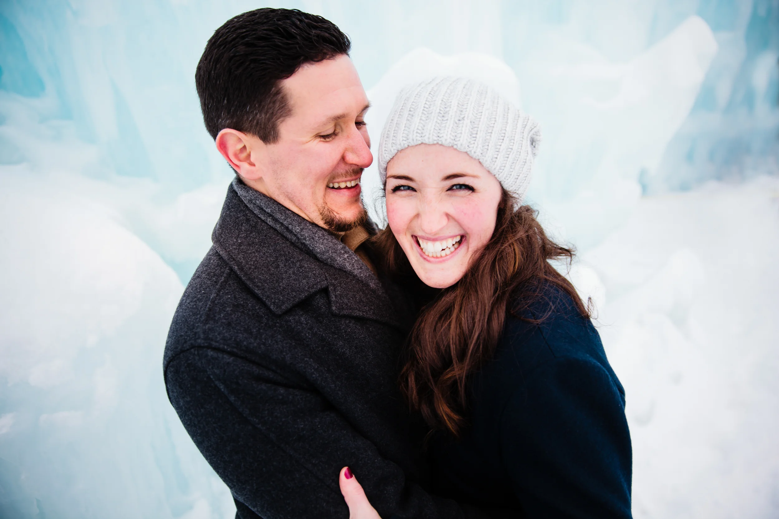 A couple smiling and hugging in a snowy, icy landscape, with a background of large ice formations.
