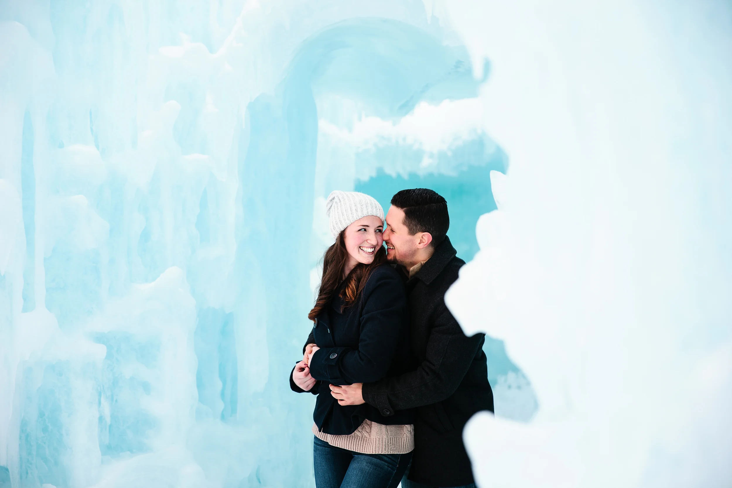 A smiling woman and man embracing each other inside an icy, snow cave, with ice formations around them.