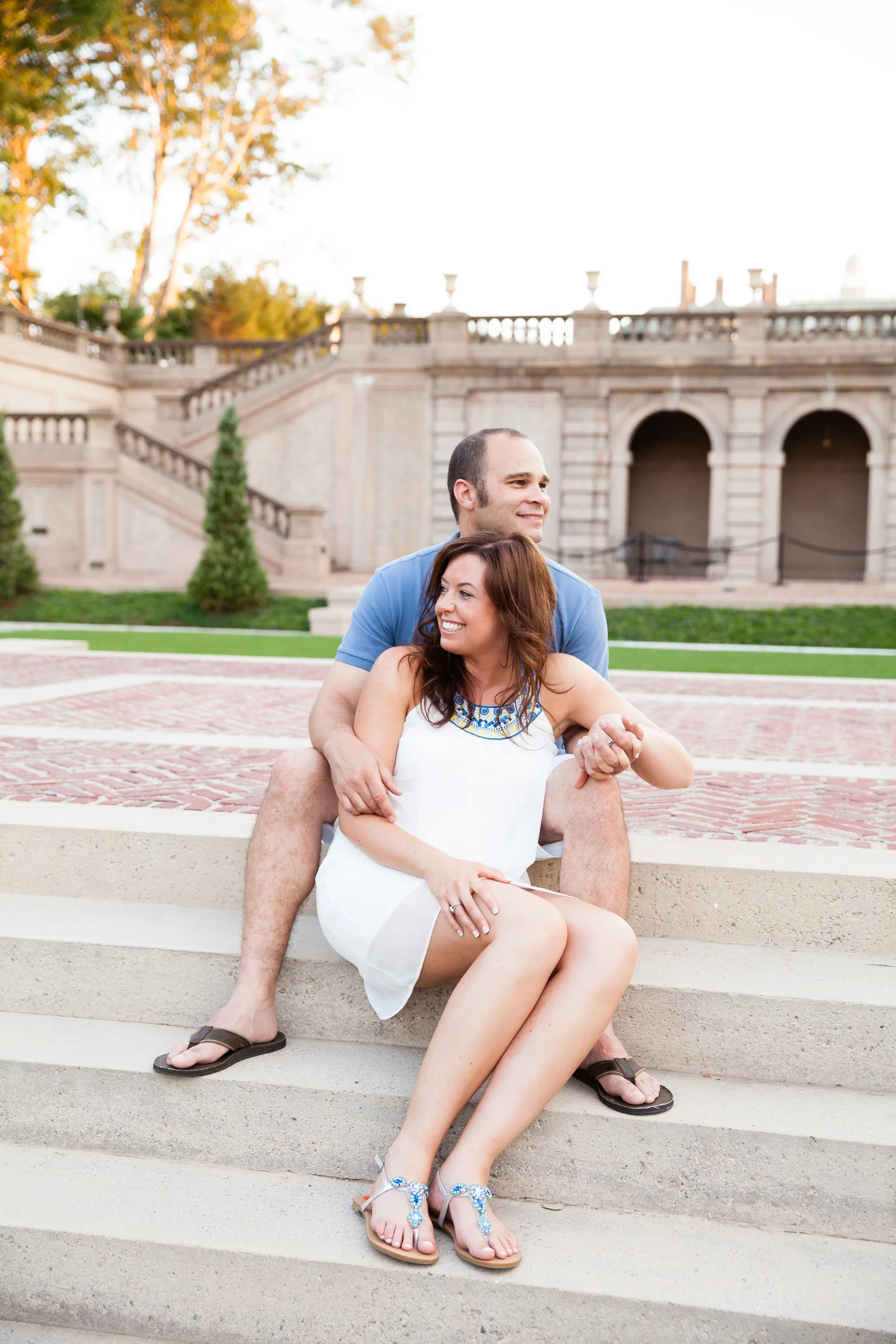 A smiling woman and man sitting on outdoor steps with ancient-style architecture in the background.