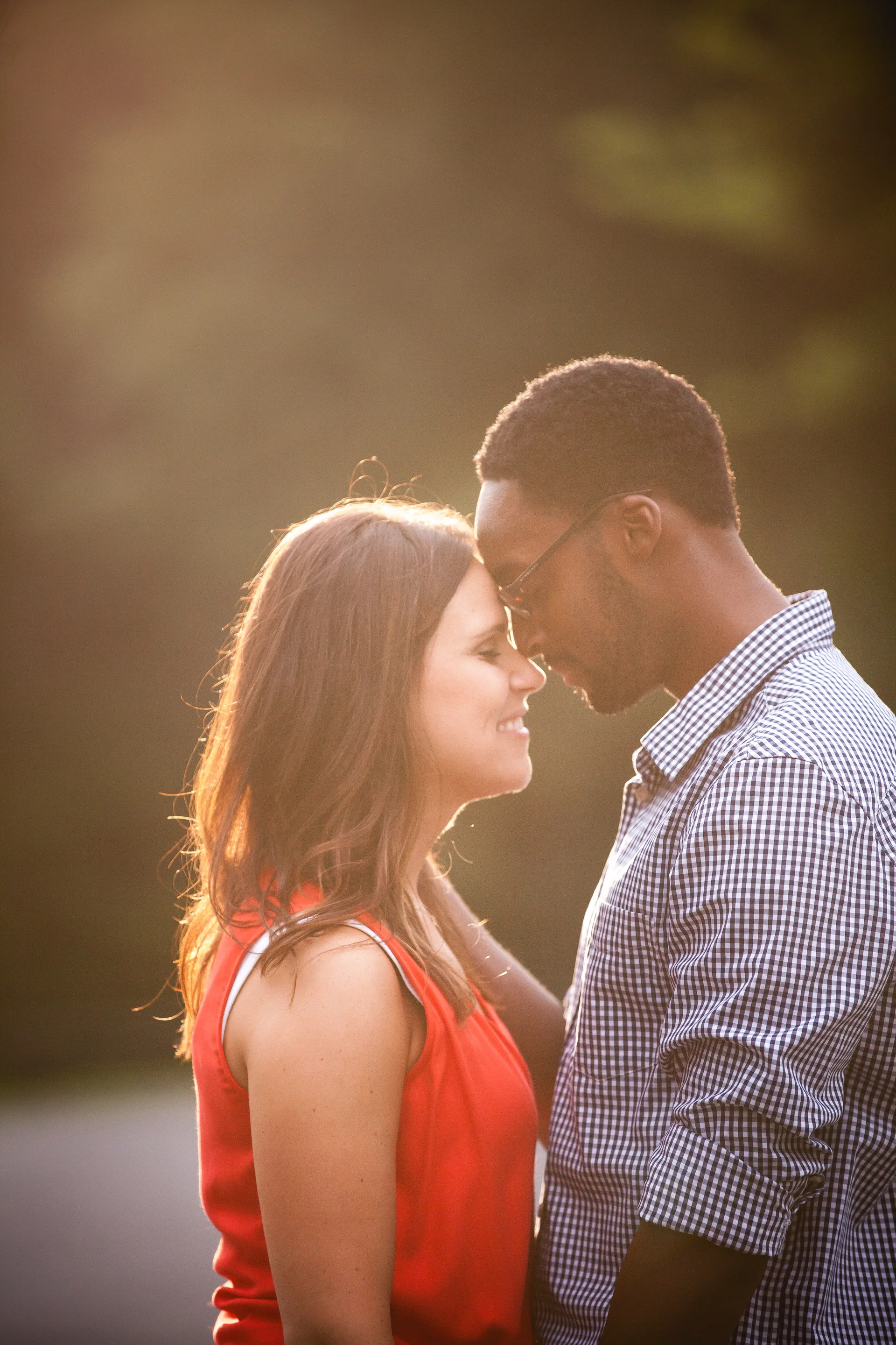 A couple with foreheads touching, smiling, standing outdoors during sunset.