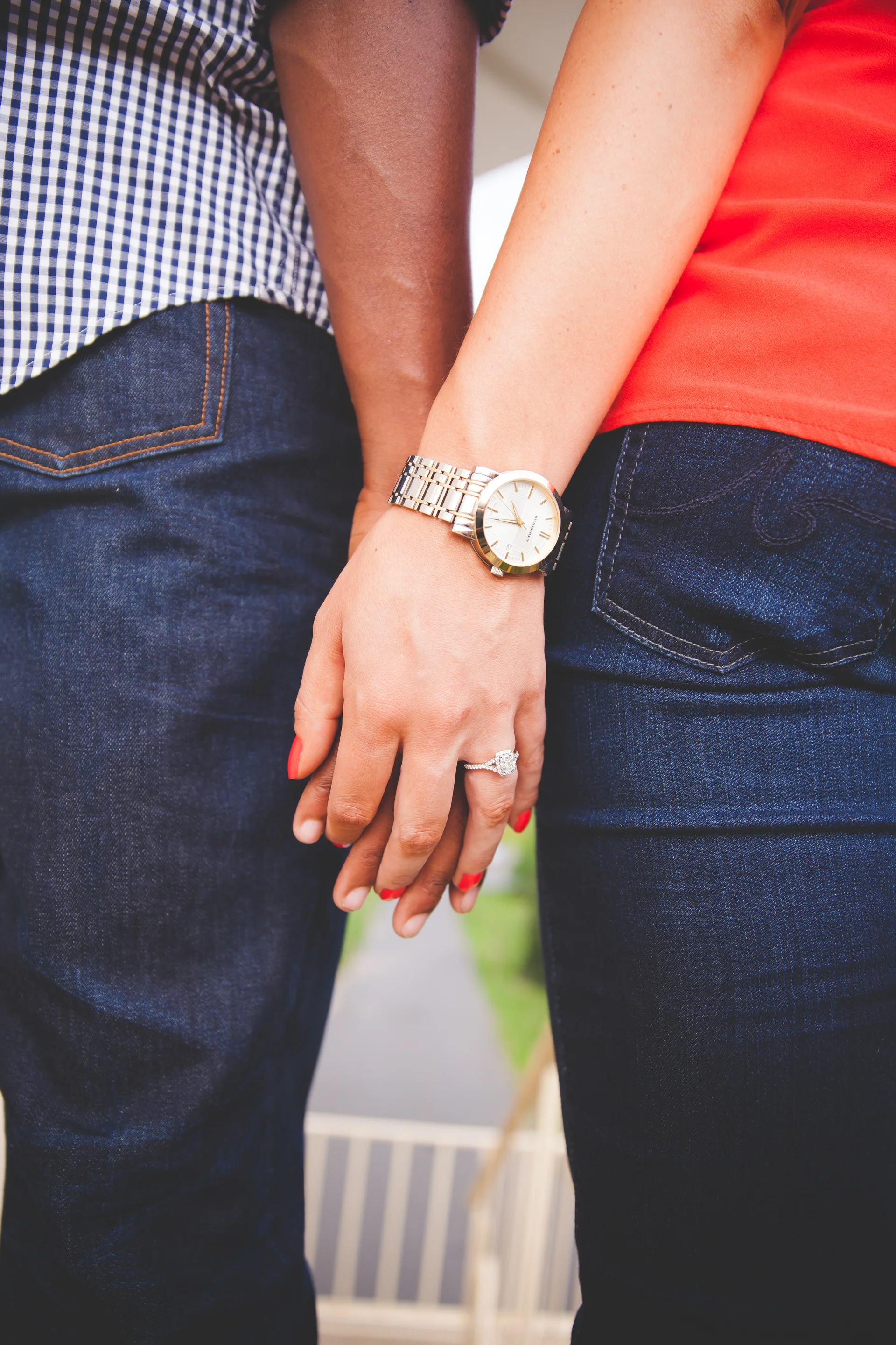 Close-up of two people standing close, with one person wearing a watch and a ring, and the other person's hand resting on the first person's thigh.