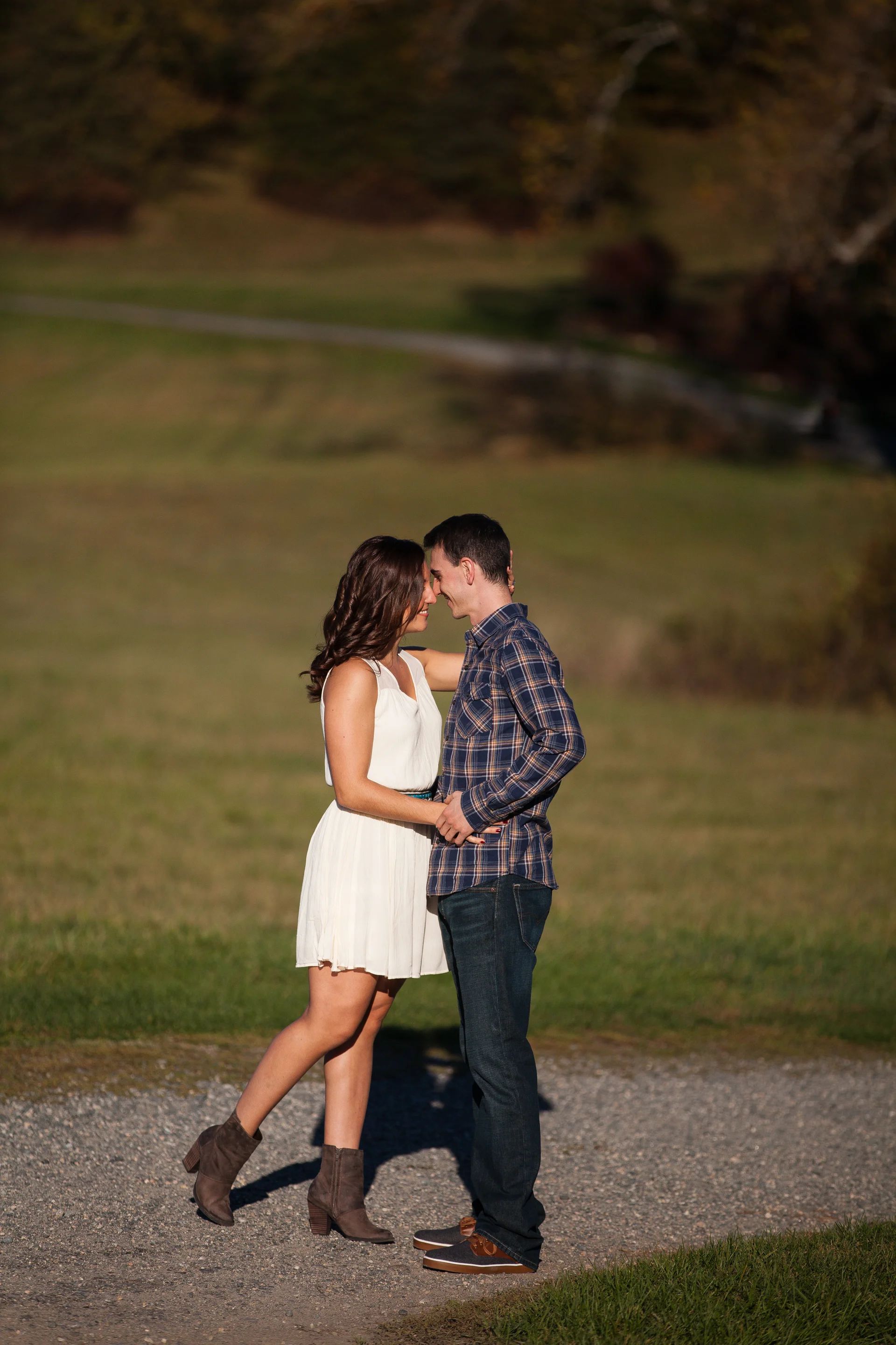 A couple standing close together outdoors, about to kiss, with a scenic background of a grassy field and trees.