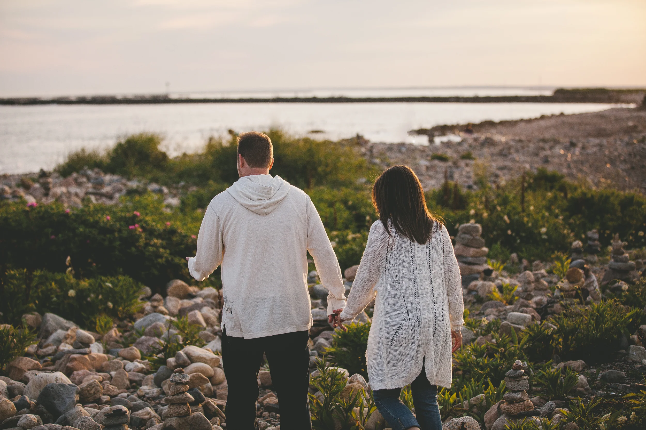 A couple walking hand in hand on a rocky beach near water at sunset.