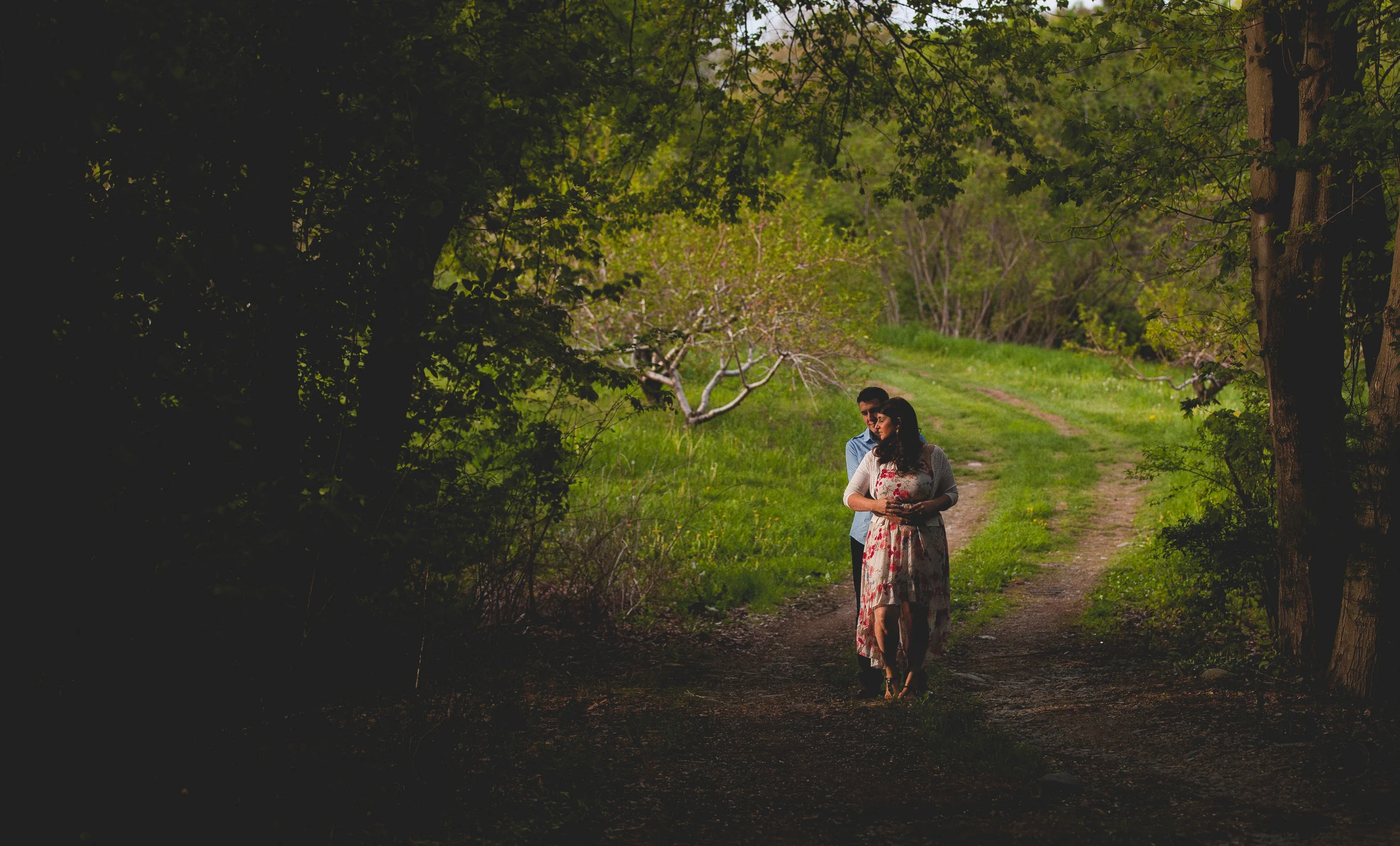 A couple walking on a dirt path through a lush green forest during daytime.