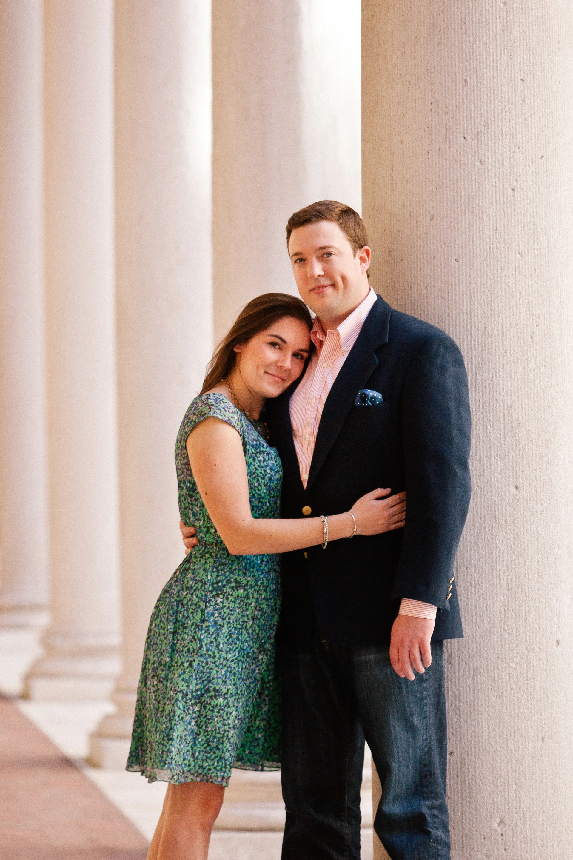 A young couple standing close together near large columns, smiling at the camera outside a building with classical architectural features.