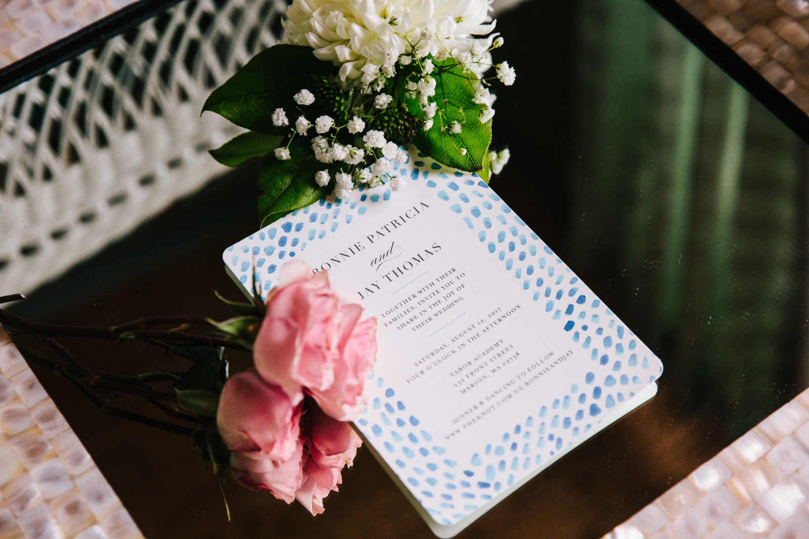 Wedding invitation card with pink roses and white flowers on a dark table.