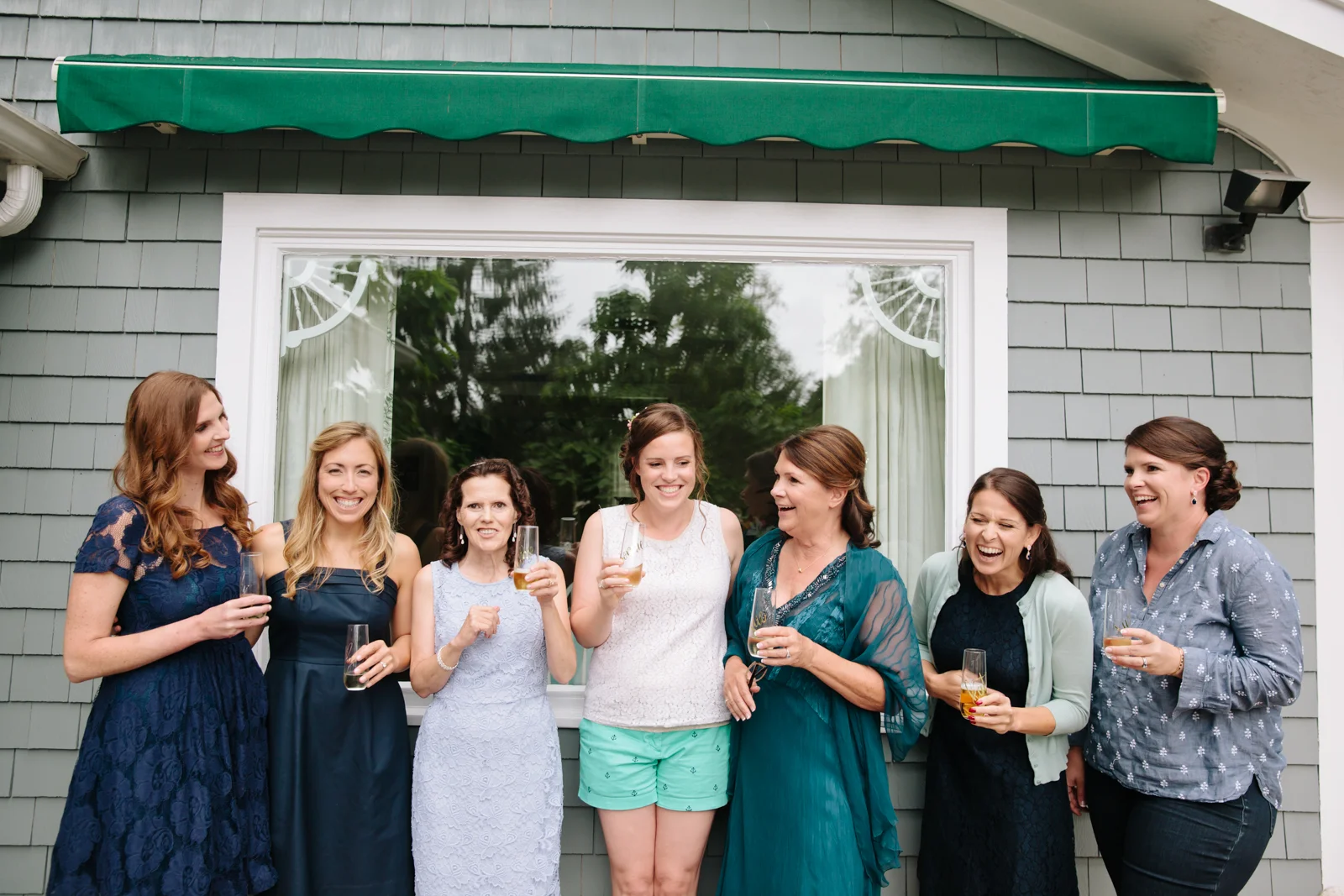 A group of seven women standing outside a building, holding drinks, and smiling.