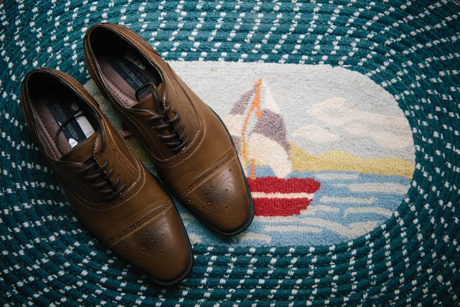 Brown leather dress shoes on a nautical-themed rug with a sailboat and lighthouse design