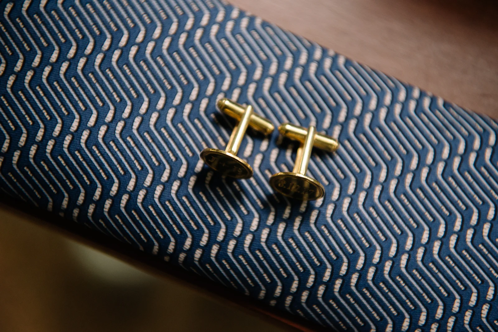 A pair of gold cufflinks resting on a patterned blue and white fabric.