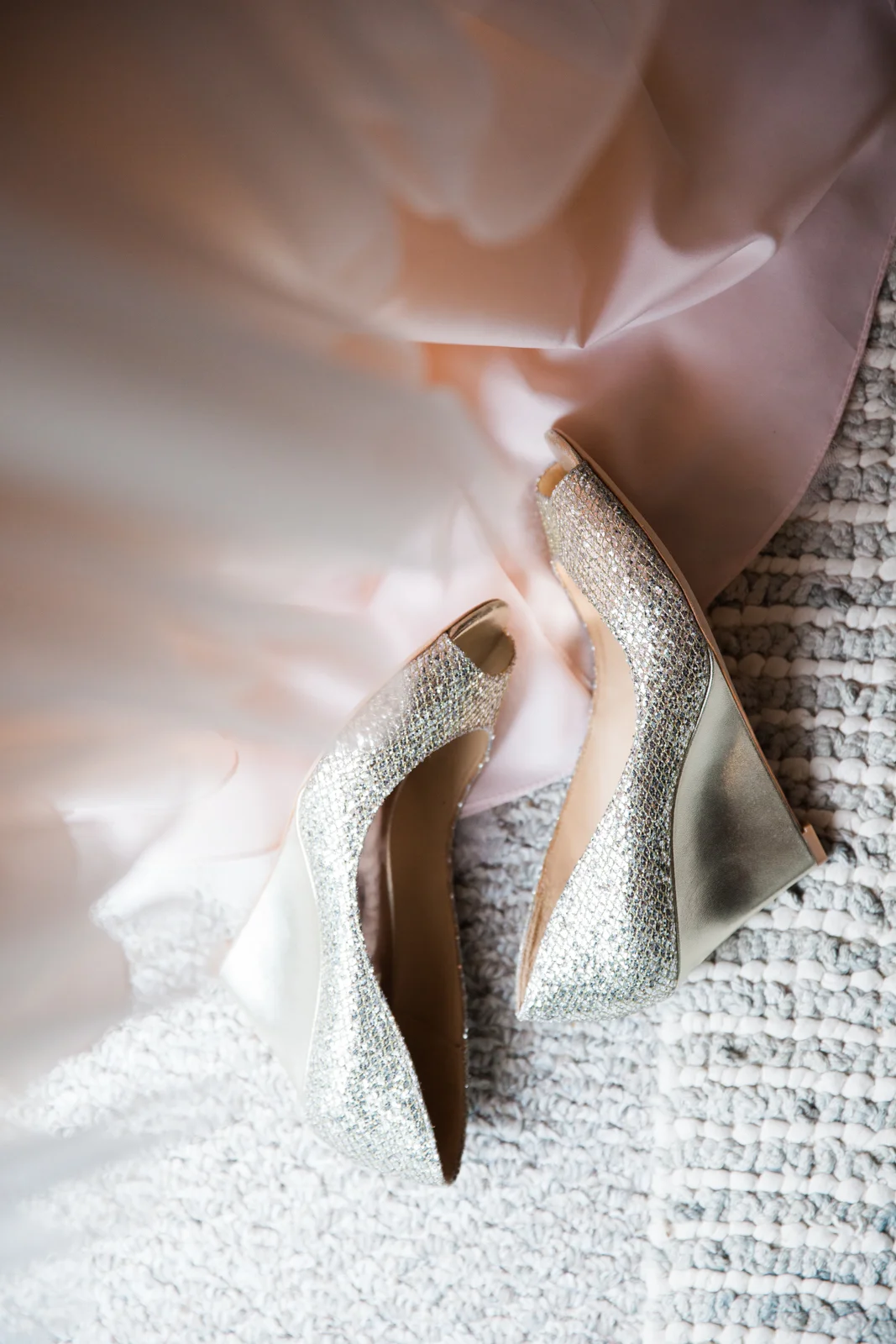 A pair of glamorous high-heeled shoes covered in sparkling rhinestones placed on a textured carpet.