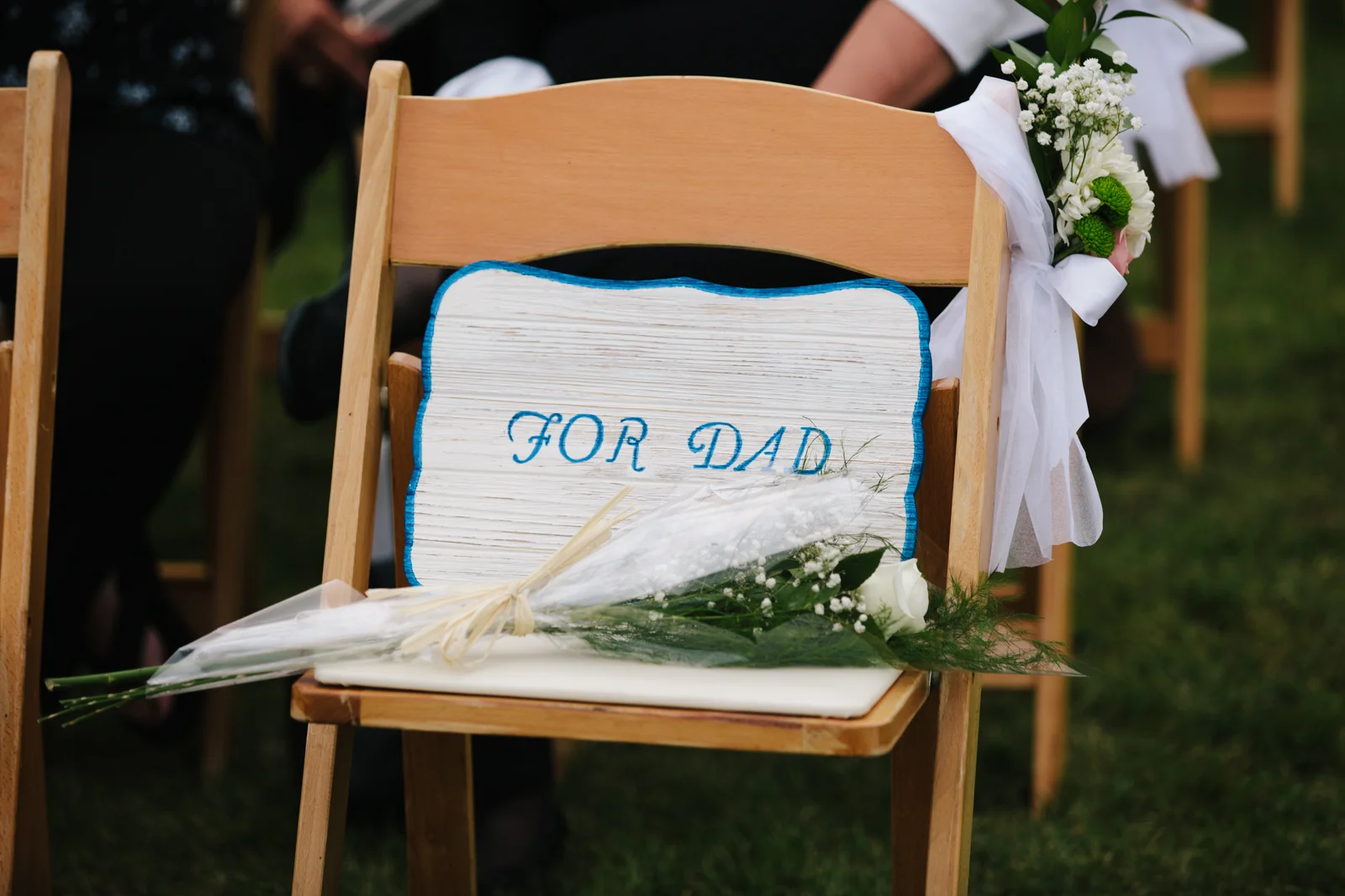 Wooden chair decorated with flowers and a sign that reads 'For Dad' for a wedding or event.