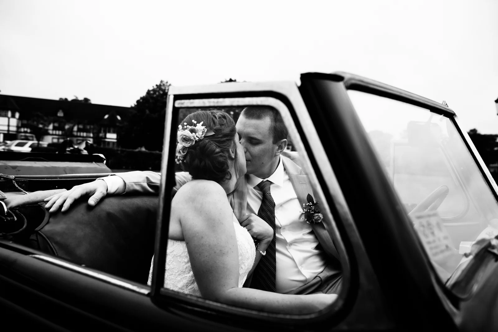 Black and white photo of a newlywed couple kissing in the backseat of a vintage car.