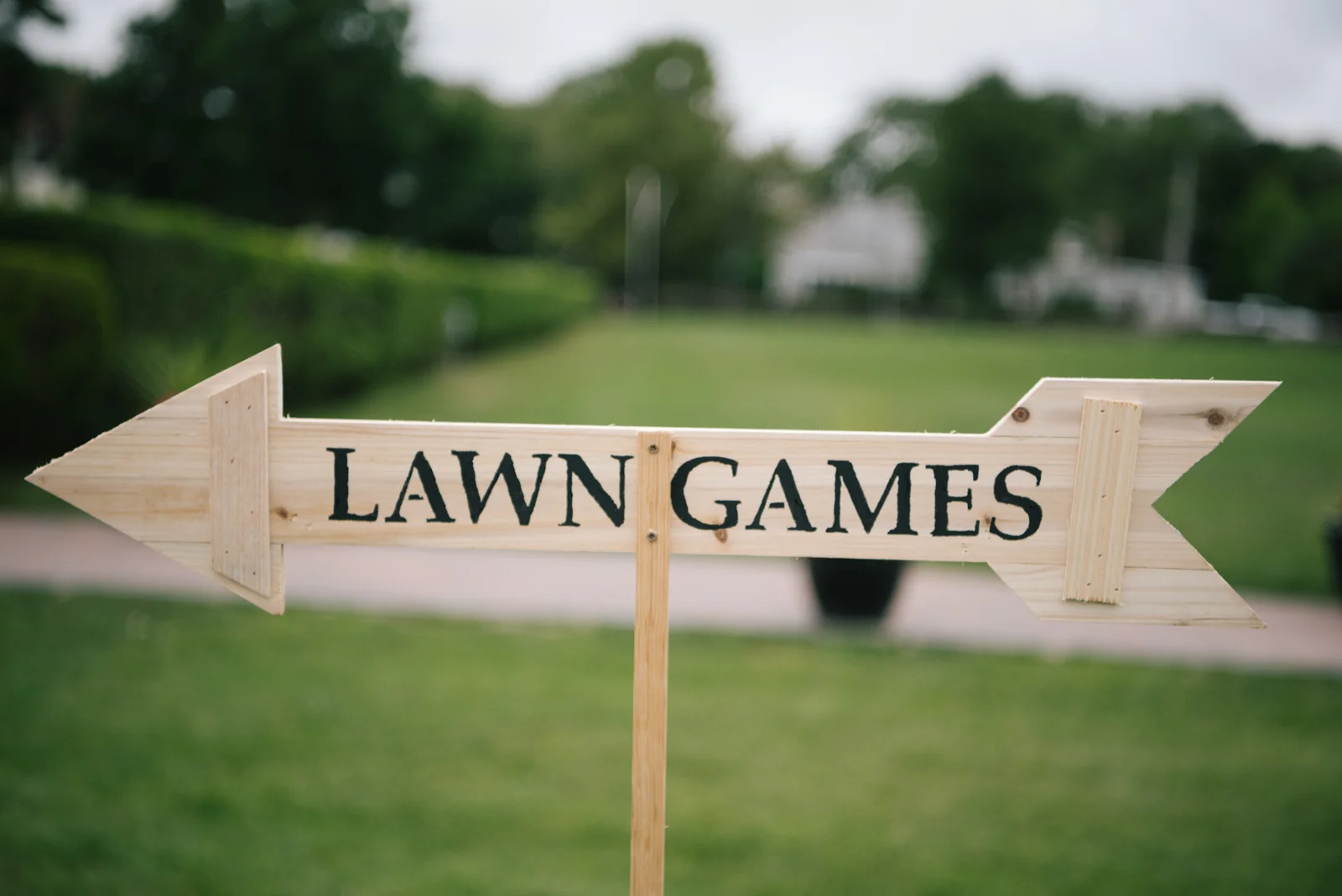Wooden sign shape pointing left and right with the words "Lawn Games" painted on it, placed outdoors on a grassy area.