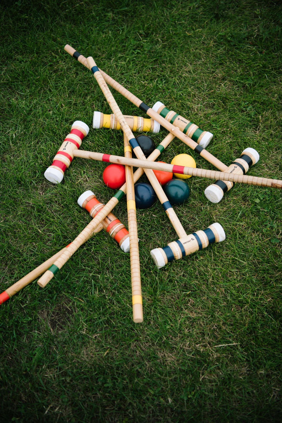 Colorful lawn game equipment scattered on grass, including wooden mallets and balls, used for croquet.